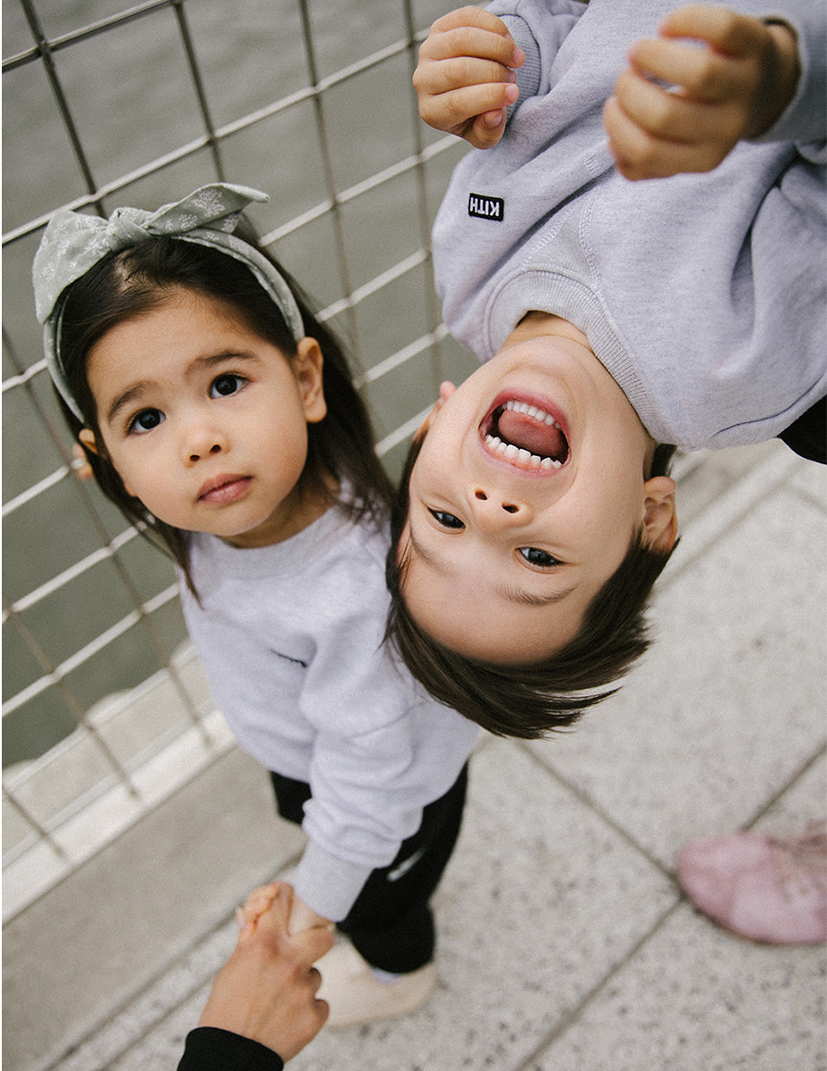 Niño y niña riendo boca abajo mientras el padre los sujeta en la calle, sesión de fotografía infantil espontánea