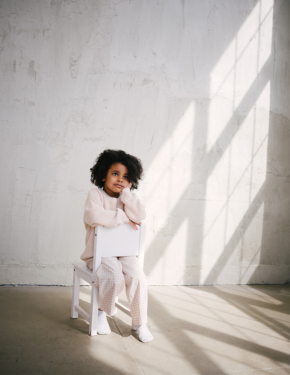 Niña sentada en silla junto a ventana con luz natural, sesión de fotografía infantil en estudio